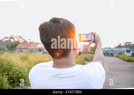 un uomo che sta scattando foto di se stesso e della natura in vari stili. quell'uomo ha le spalle alla telecamera. immersi nella natura in un pomeriggio di sole. Foto Stock