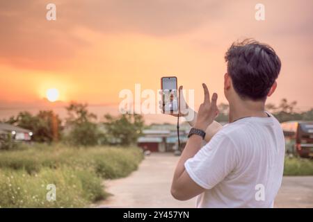 un uomo che sta scattando foto di se stesso e della natura in vari stili. quell'uomo ha le spalle alla telecamera. immersi nella natura in un pomeriggio di sole. Foto Stock