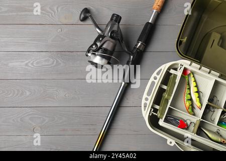 Diversi attrezzi da pesca in scatola e canna con rullo rotante su tavolo in legno grigio, vista dall'alto. Spazio per il testo Foto Stock