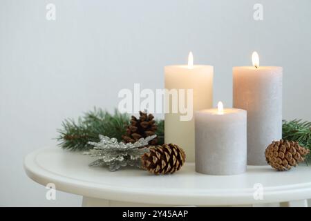 Bruciare candele e rami di abete sul tavolino da caffè vicino alla parete luminosa, spazio per il testo Foto Stock