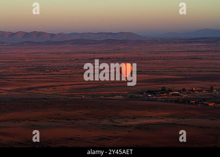 Sorvolando il deserto marocchino, il vibrante palloncino arancione danzerà con la luce dell'alba, dipingendo il cielo con calore e meraviglia Foto Stock