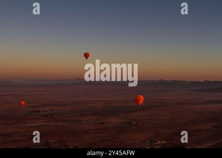 Tre vivaci palloncini arancioni scivolano graziosamente sul vasto deserto marocchino. Foto Stock