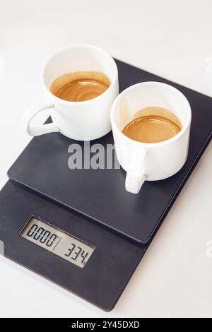 Vista dall'alto di due tazze da espresso con crema ricca bilanciata in scala che mostra il peso preciso della bevanda pronta Foto Stock