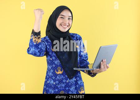 Donna indonesiana ASN o funzionario pubblico eccitata mentre tiene in mano un laptop, con indosso l'uniforme blu Korpri. PNS Indonesia Concept Foto Stock