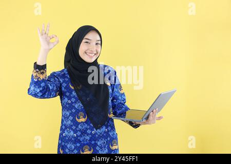 Donna indonesiana ASN PNS che tiene un computer tablet portatile con gesto OK, con indosso l'uniforme Hijab e Korpri Foto Stock
