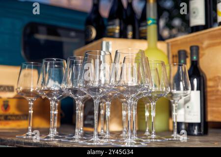 Bicchieri da vino vuoti allineati sul tavolo, bicchieri disposti in modo ordinato, bottiglie di vino sullo sfondo, preparazione per la degustazione di vini, concetto Foto Stock