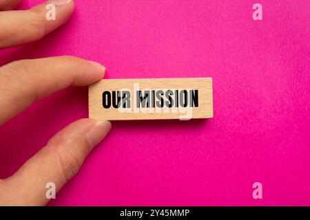 Il nostro messaggio di missione scritto su un blocco di legno con sfondo rosa. Concettuale il nostro simbolo della missione. Copia spazio. Foto Stock