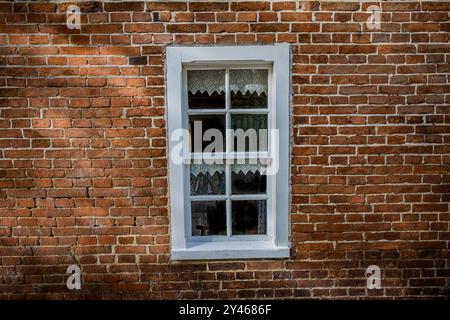 Finestra in vecchio stile con cornice bianca e tende in pizzo su un muro di mattoni rossi Foto Stock