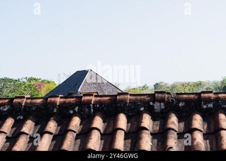 Vista ravvicinata di un tetto in terracotta intempestivo con piastrelle irregolari. Mancano alcune tessere, rivelando un buco sotto. La superficie mostra segni di usura Foto Stock