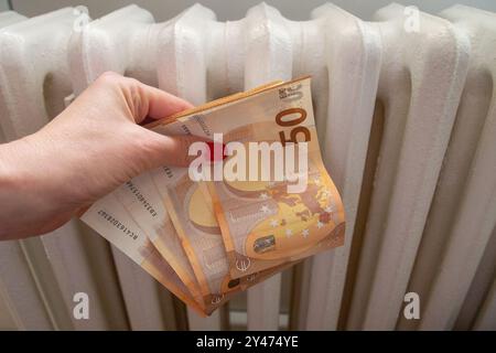 La mano di una donna tiene i soldi nxt per il riscaldamento dei radiatori come concetto per i costi crescenti Foto Stock