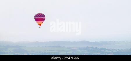 Mongolfiera rossa che vola in alto sui livelli del Somerset con bruciatore acceso molto presto la mattina in una giornata molto nebulosa e noiosa, nel Regno Unito Foto Stock