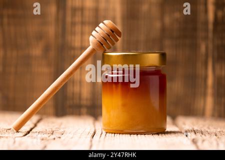 Miele di grano saraceno in un vaso e un cucchiaio di legno su fondo di legno. Foto Stock