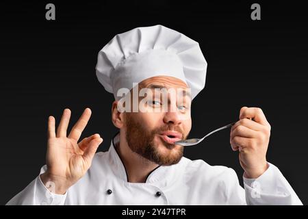 Lo Chef degustazione e approvazione di cibo cucchiaio di contenimento in posa di Studio Foto Stock