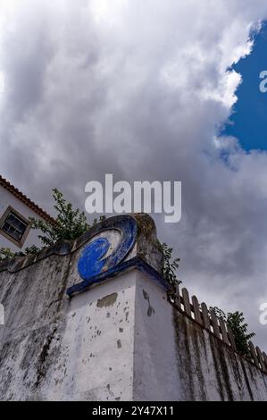 Le pareti intemprate con un dettaglio blu a turbolenza si stagliano contro un cielo dolente a Óbidos Foto Stock