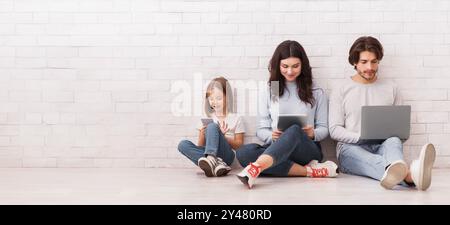 Felice famiglia di tre seduti al piano con diversi gadget Foto Stock