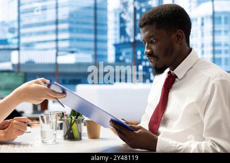 Dipendenti delle risorse umane che implementano una strategia di reclutamento per l'azienda in materia di diversità e inclusione. Reclutatori che fanno un colloquio con un uomo afroamericano per affari inclusivi, offrendo un contratto Foto Stock