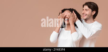 Ragazzo amorevole che sorprende la sua ragazza, coprendo gli occhi con le mani Foto Stock