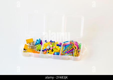 Graffette e graffette in carta colorata in una scatola di plastica chiusa a chiave su una superficie bianca Foto Stock