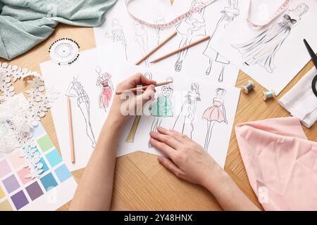 Stilista che disegna uno schizzo di un bellissimo vestito al tavolo di legno, vista dall'alto Foto Stock