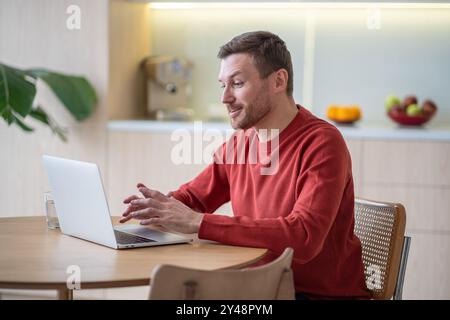 L'uomo contento ha gesticolati di videochiamata per riunioni online che guardano lo schermo di un notebook seduto a casa Foto Stock