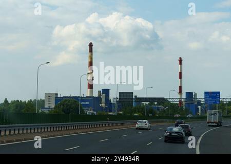 Gliwice, Polonia - 15 giugno 2023: L'animata area industriale di Gliwice presenta torreggianti ciminiere sullo sfondo di morbide nuvole, mentre il veicolo Foto Stock