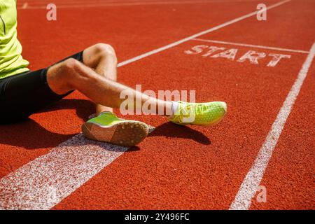 Primo piano di gamba e piede di un corridore su una pista atletica rossa, posizionata vicino alla linea di partenza contrassegnata con la parola "START". Il corridore indossa bri Foto Stock