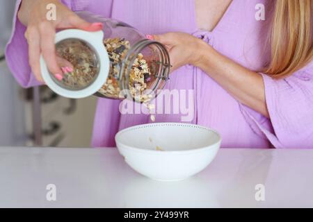 la colazione sana le mani femminili mettono la muesola fatta in casa in un piatto Foto Stock