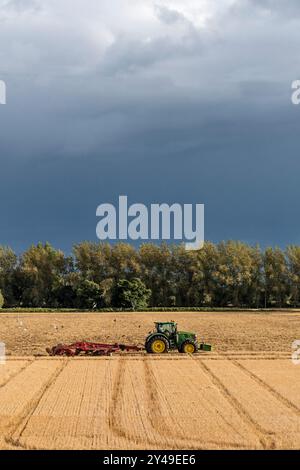 Trattore John Deere 8400R che tira un coltivatore Horsch Tiger MT davanti a un cielo buio e tempestoso in un'azienda agricola di Norfolk Foto Stock