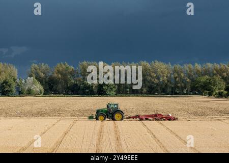 Trattore John Deere 8400R che tira un coltivatore Horsch Tiger MT davanti a un cielo buio e tempestoso in un'azienda agricola di Norfolk Foto Stock