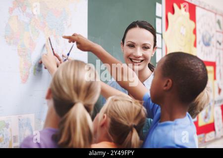 Insegnanti, bambini e apprendimento geografico sulla mappa per l'istruzione, la scienza o gli studenti studiano il pianeta in classe. Donna felice, gruppo e lezione per il mondo Foto Stock