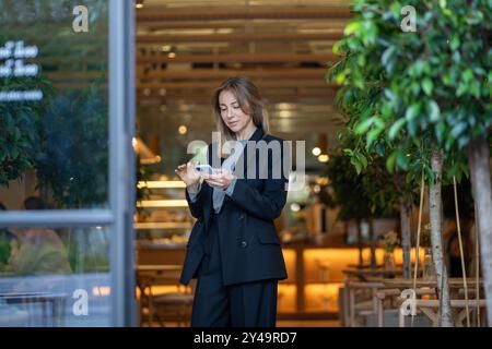 Donna d'affari che chatta su Internet su smartphone, gestisce contratti e corrispondenza in corridoio Foto Stock