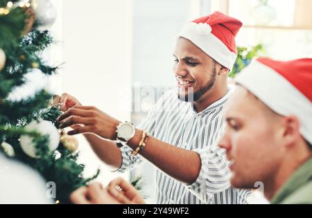 Uomo felice, amici e albero con decorazioni per natale, festività o festeggiamenti in ufficio. Giovani, uomini o colleghi che aiutano con le decorazioni Foto Stock