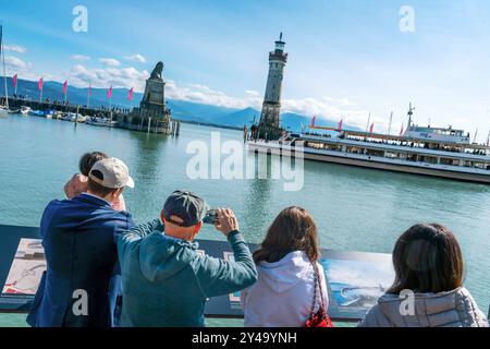 Touristen fotografieren die berühmte Lindauer Hafeneinfahrt, als ein Schiff der Bodenseeflotte den Hafen verlässt, Bodensee, Lindau, settembre 2024 Deutschland, Lindau, settembre 2024, Touristen fotografieren die bekannte Lindauer Hafeneinfahrt, Leuchtturm und Bayerischer Löwe, ein Schiff der Bodenseeflotte verlässt den Hafen, Blick von Lindau Insel auf den Bodensee, bestes Wetter, blauer Himmel, Alpenkette am Horizont, die historische Hafeneinfahrt wurde 1856, Spätsommer la famosa nave turistica del porto di Lindmus *ert, il porto di lindauer, il porto di Herbestau Foto Stock