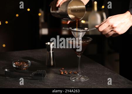 Il barista prepara deliziosi martini espresso al tavolo scuro contro le luci sfocate e i primi piani Foto Stock