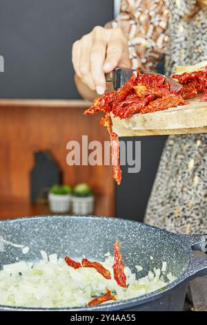 I pomodori secchi vengono aggiunti a una padella con cipolle per una salsa ricca e saporita Foto Stock