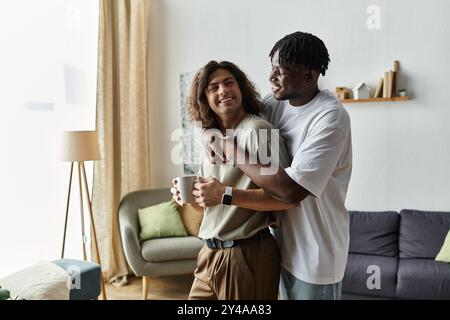 Due partner condividono un caldo abbraccio mentre ridono, sorseggiano un caffè e si godono la loro casa. Foto Stock