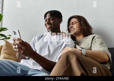 Due partner si siedono a stretto contatto su un divano, condividendo un momento di gioia mentre guardano lo schermo di un telefono. Foto Stock