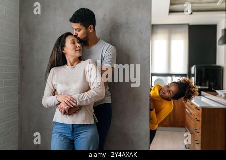 La bella coppia multietnica passa del tempo insieme, abbracciando e sorridendo con il bambino sullo sfondo Foto Stock