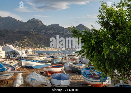 Vista panoramica dei pescherecci abbandonati a Giardini Naxos, in Sicilia, con Taormina arroccata sulla collina sullo sfondo. Paesaggio costiero mediterraneo Foto Stock