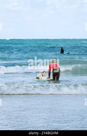 Un giovane surfista principiante con un istruttore di surf che impara a fare surf a Towan Beach a Newquay in Cornovaglia nel Regno Unito. Foto Stock
