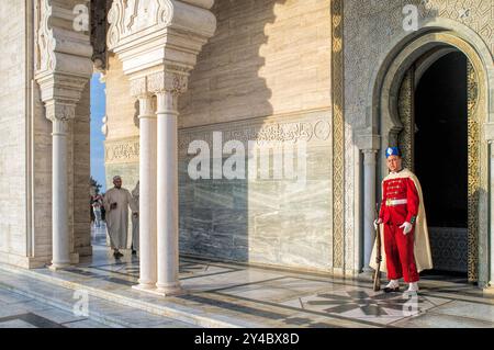 Rabat, Marocco, 24 aprile 2015, Una guardia assiste al Mausoleo di Mohammed V, con un visitatore che cammina sul pavimento in marmo lucido, come il sole Foto Stock