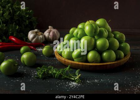 Tkemali, prugna verde ciliegia, con ingredienti per salsa, coriandolo, menta, peperoncino, aglio, su un tavolo di legno, primo piano, rustico, cibo di fondo, no p Foto Stock