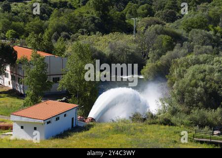 Edificio circondato dal verde della natura e da un potente flusso d'acqua che scorre da un serbatoio, il serbatoio di Embalse de Plasencia, Embalse de Jerte, Rio Je Foto Stock