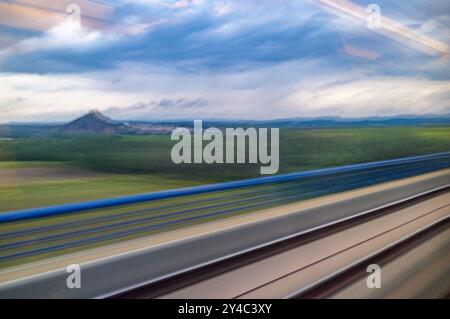 Vista panoramica dalla finestra di un treno AVE ad alta velocità che corre attraverso Cordova, Andalusia, Spagna. Lussureggianti paesaggi verdi e montagne lontane sotto a. Foto Stock