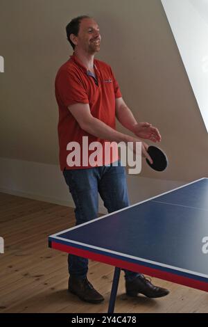 Un bell'uomo di quarant'anni gioca a ping-pong in abiti casual. Chiaramente gli piace la partita Foto Stock