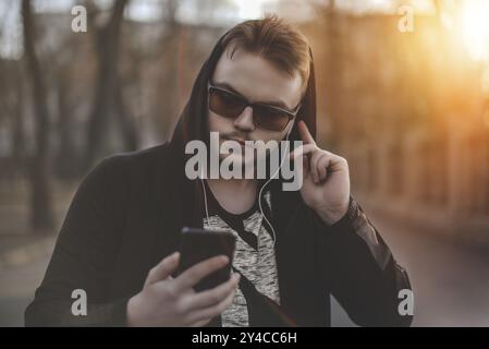 Uomo in Hood con le cuffie che guarda lo smartphone Foto Stock