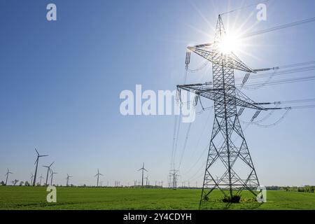 Un pilone elettrico con il sole sullo sfondo e turbine eoliche, visto in Germania Foto Stock