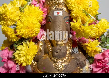 Primo piano della statua del dio indù Ganesha fatta di argilla decorata con ghirlande floreali. Foto Stock