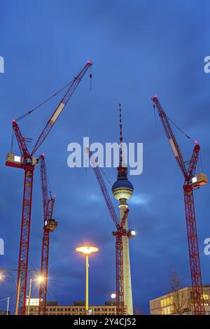 La famosa torre della televisione di Berlino di notte con quattro gru da costruzione rosse Foto Stock