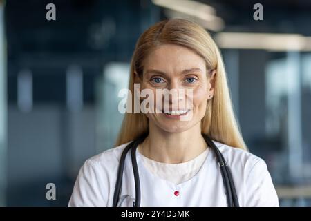 Dottoressa sicura di sé sorridente, con stetoscopio in un ufficio moderno. Rappresenta l'assistenza sanitaria, la professionalità e la fiducia nel campo medico. Foto Stock